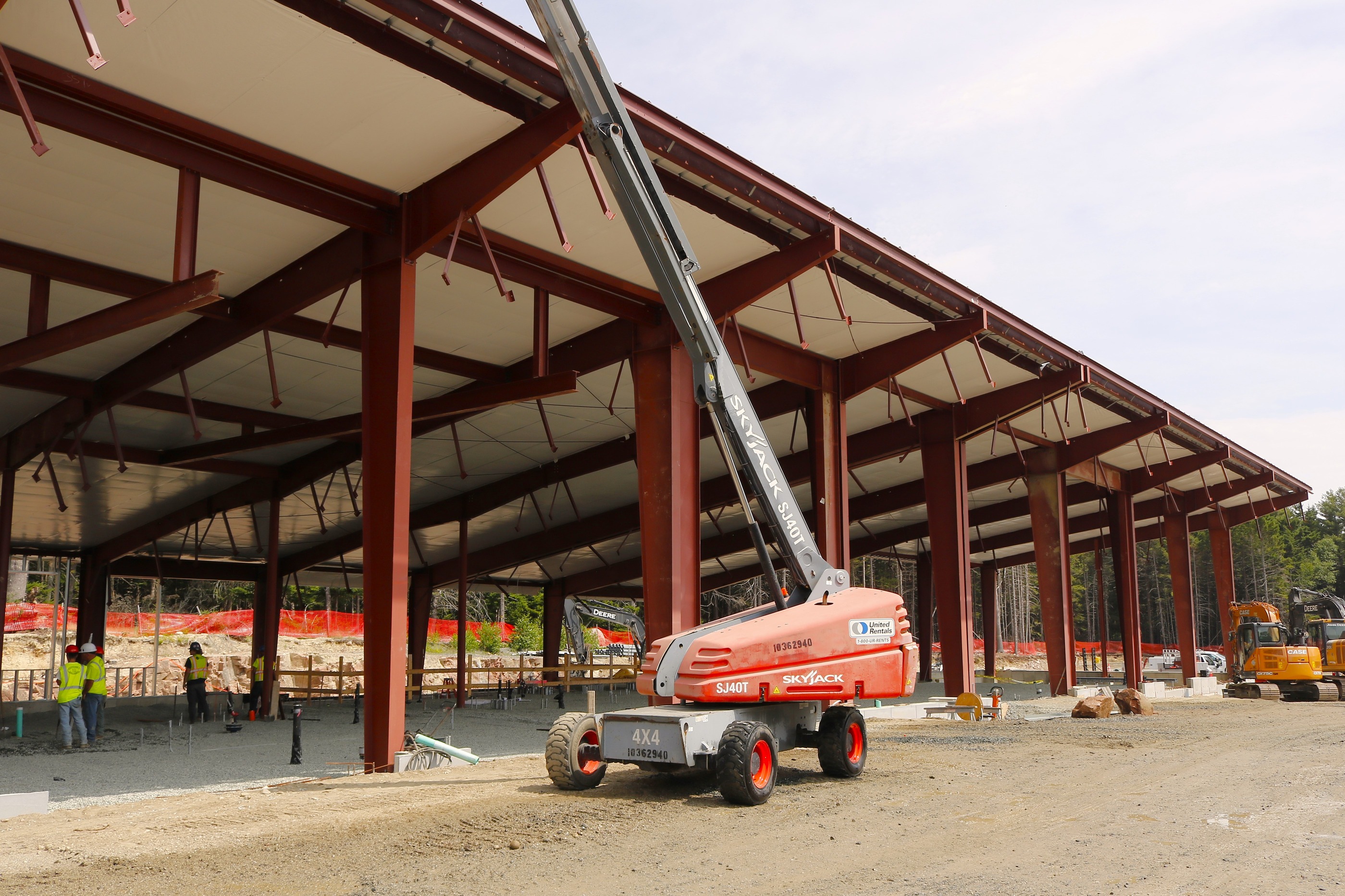 Early-stage construction of Acadia National Park's new Maintenance Building with red steel beams outlining the structure, a partial roof, and metal stud walls.