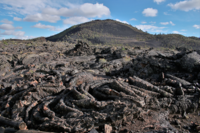 black rocks with thick wrinkly folds in front of a large cinder cone