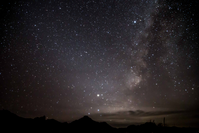 Uncountable stars and the glow of the galactic disc arc over the silhouette of a mountain range.