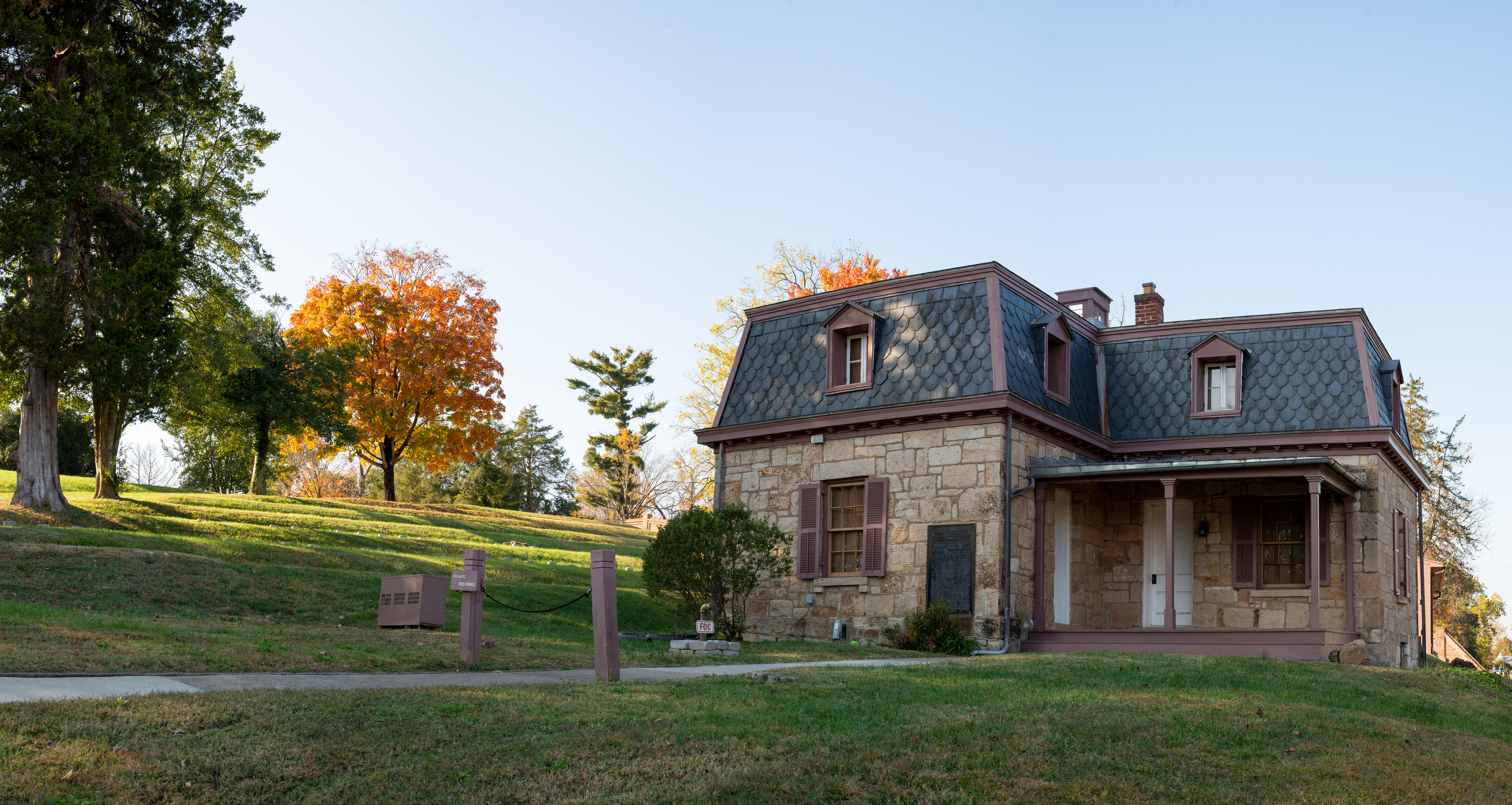 Historic structure from 1800s with stone walls and decorative slated roof next to a cemetery with some trees changing to orange fall colors.