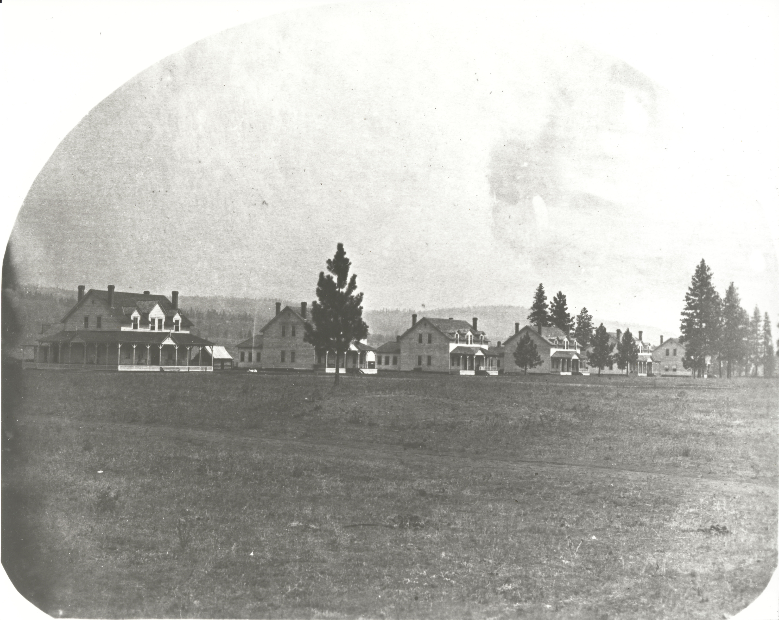 Black and white photograph of a row of white wooden houses on the edge of a field
