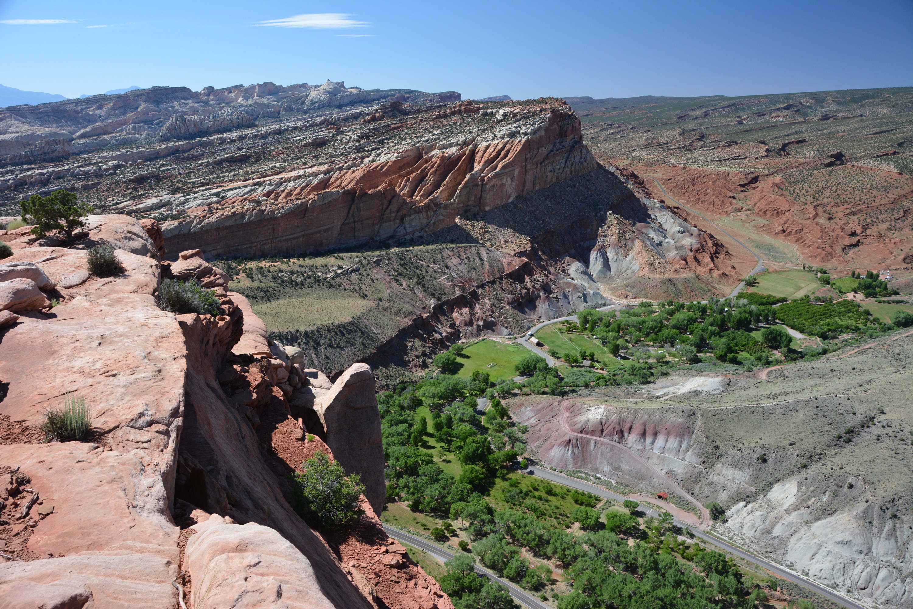 View from sandstone rim with a green valley, gray slopes, and red cliffs and blue sky. 