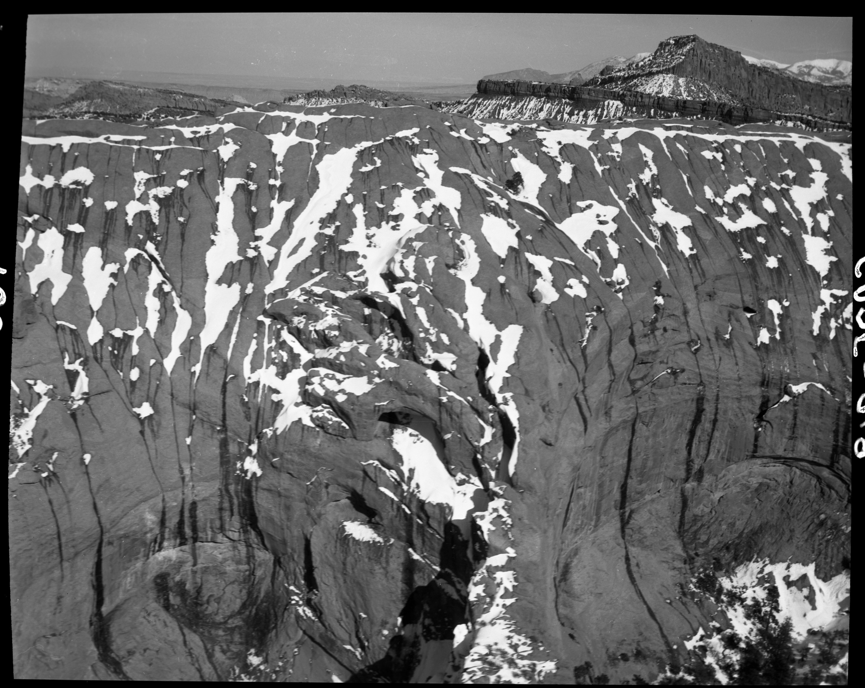 Rock cliffs partially covered in snow, with distant mountains in the background. 