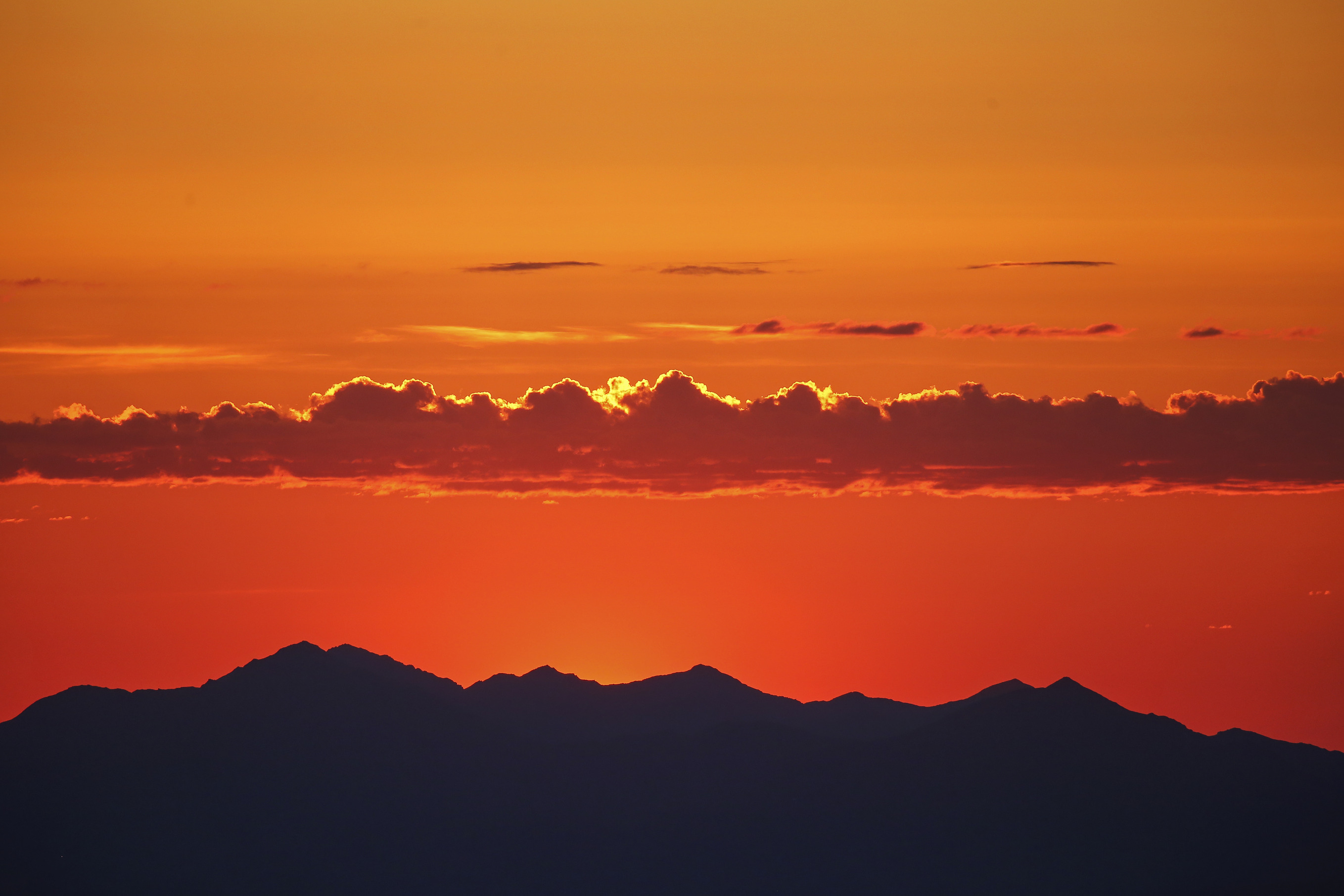 a row of clouds hanging in an orange sky over dark mountains