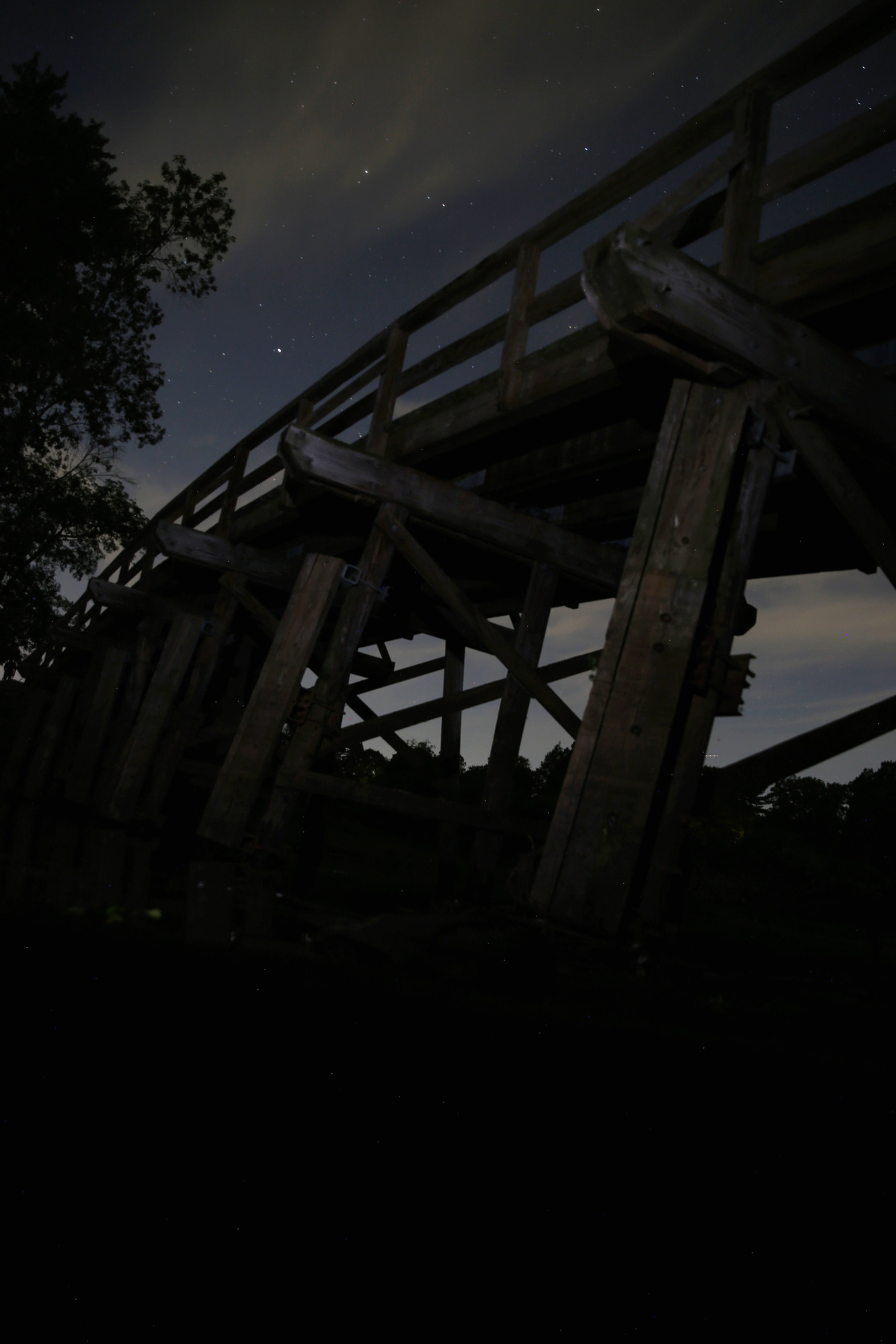 The North Bridge in Concord MA at night, under a field of stars and some light clouds.