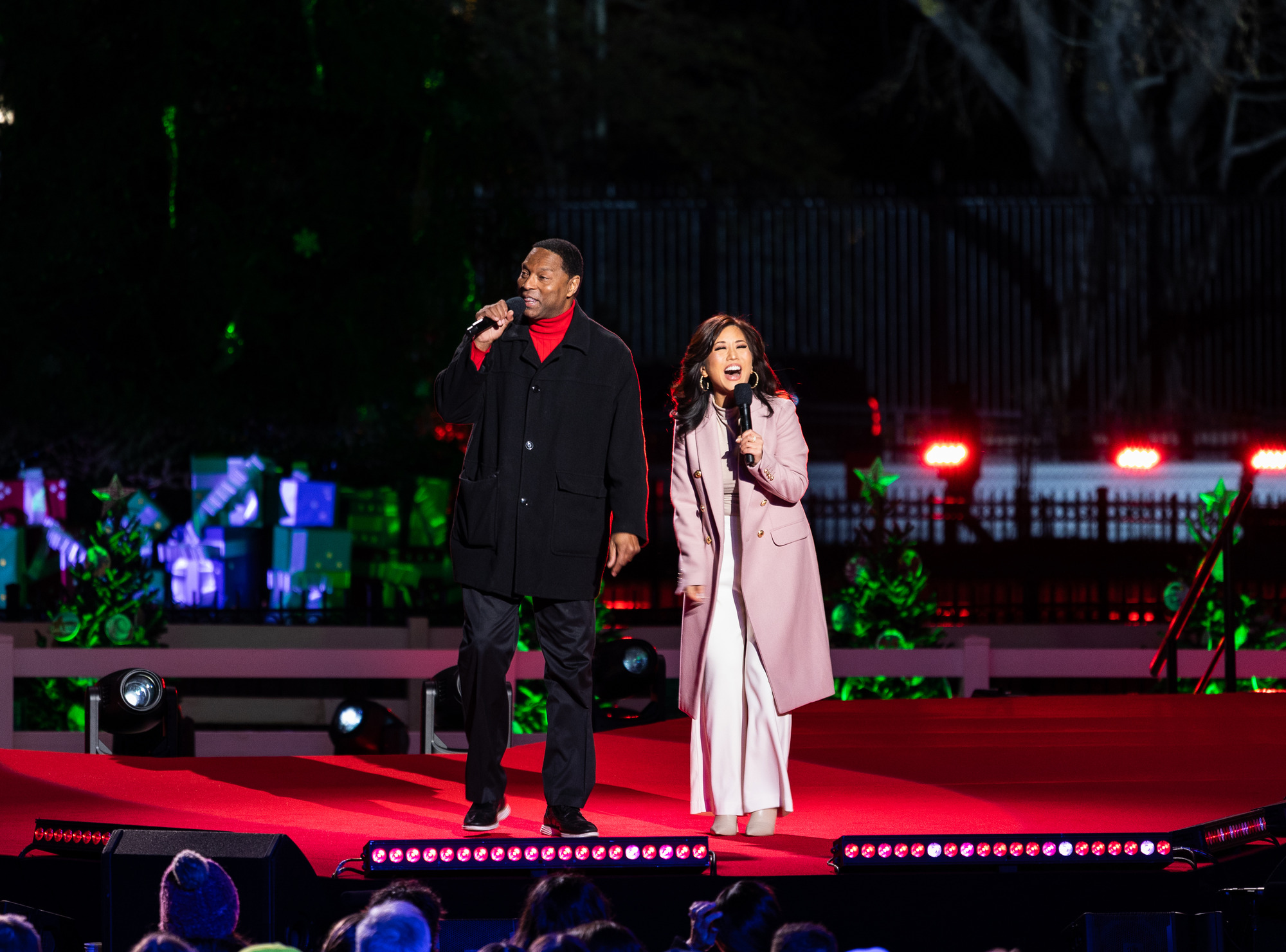 Two news anchors stand on a red stage. 