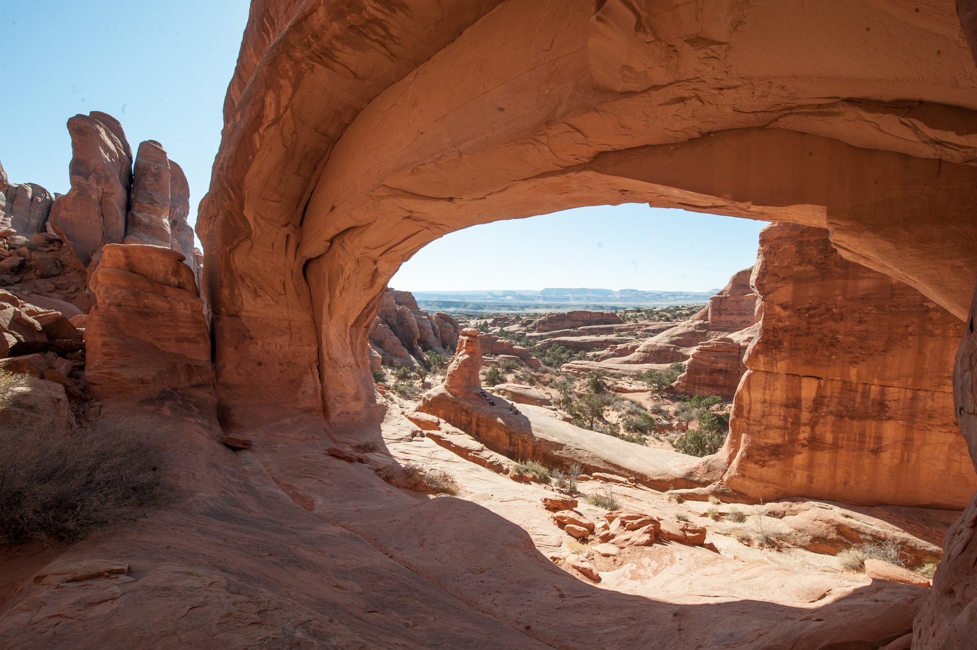 a broad stone arch with rock fins and pinnacles in the distance