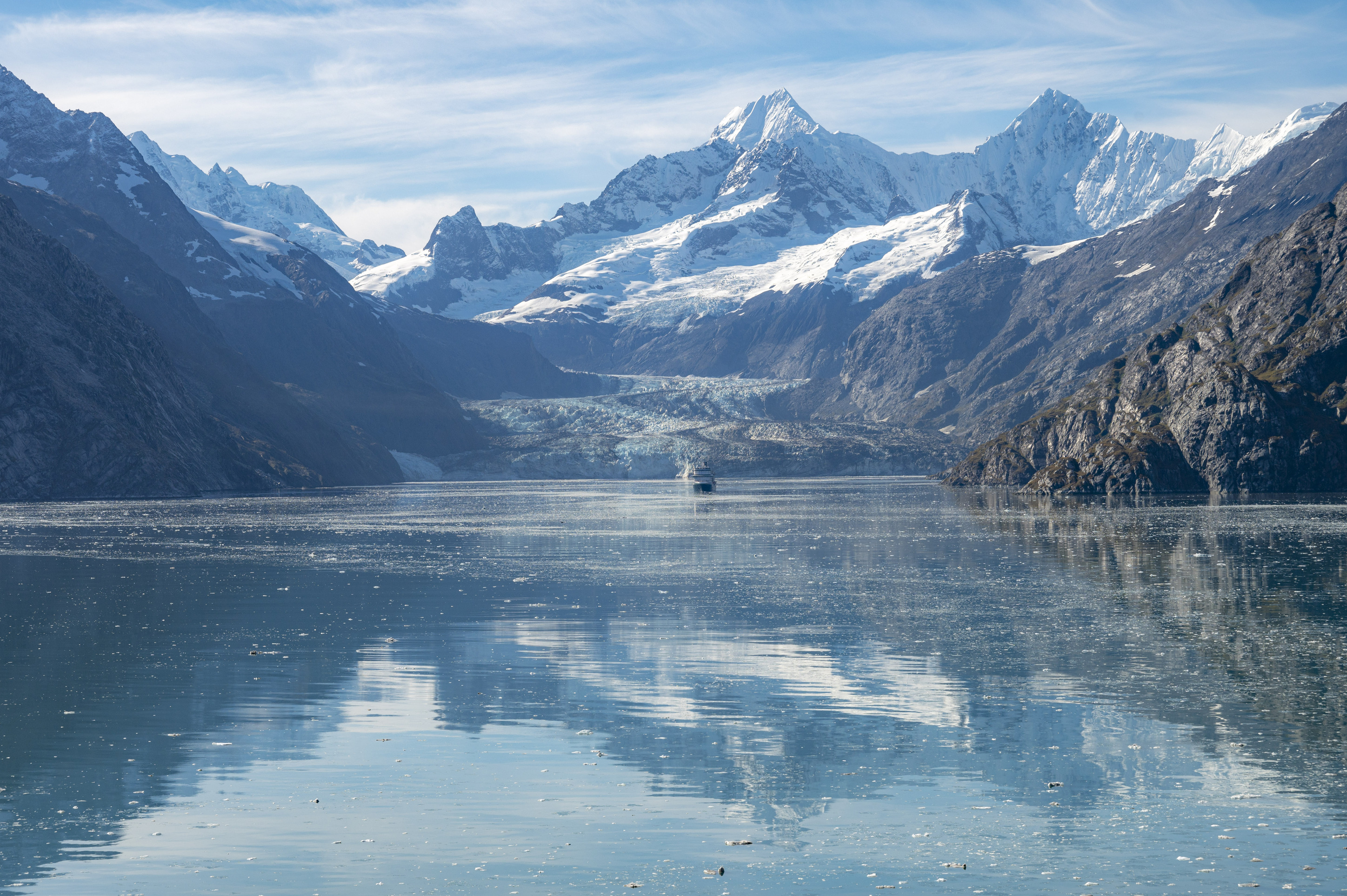 Distant view of mountains and glacier in the center of a fjord.  A large cruise ship sits in front of the glacier.