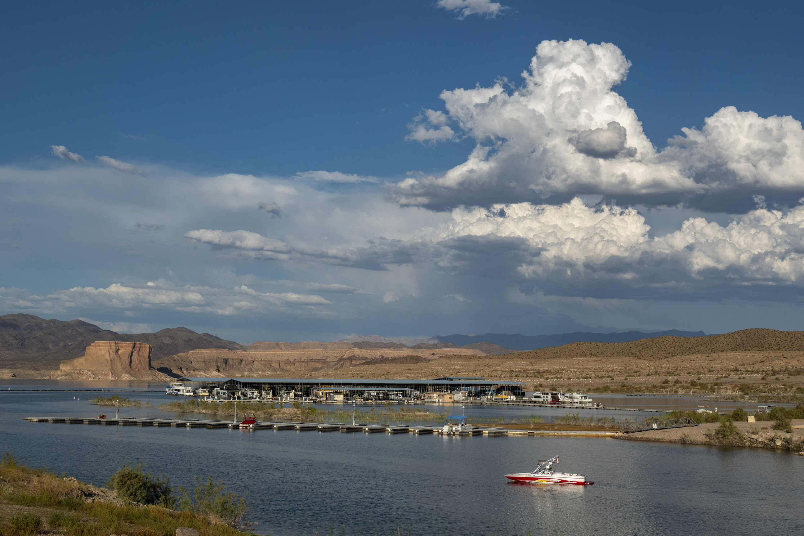 body of water, powerboat at lower right, marina, hills and cloudy sky in distance