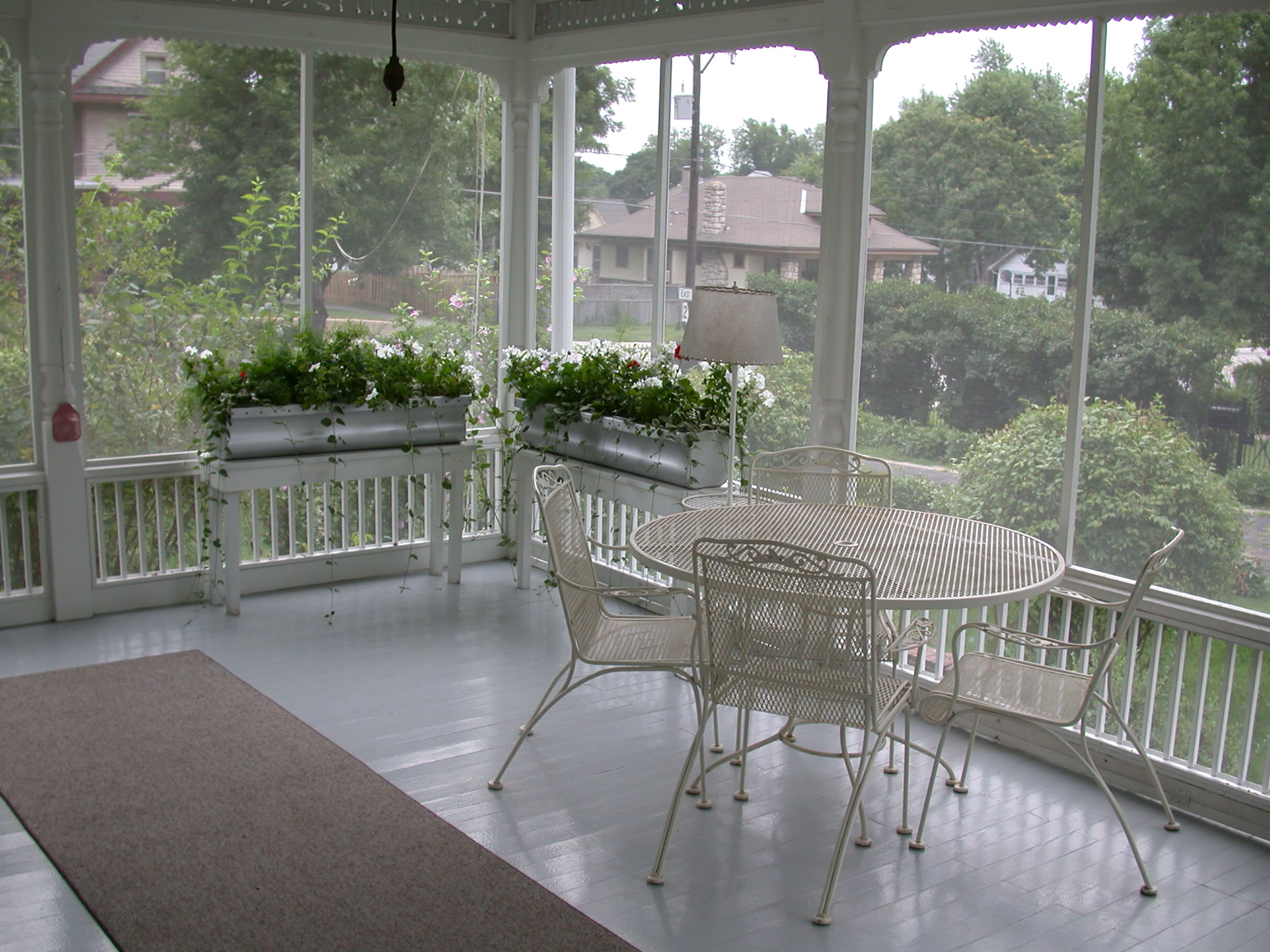 Screened in porch, with metal table and chairs, some greenery in pots.