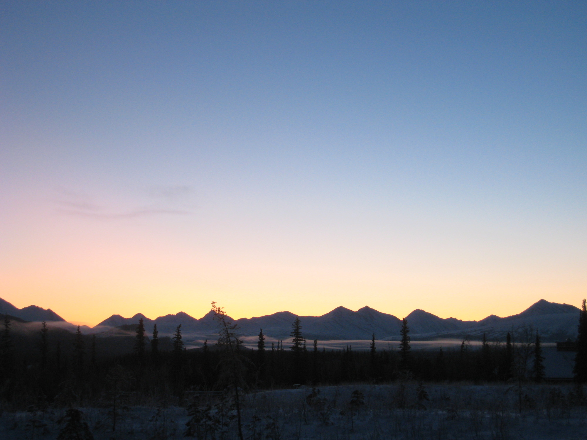 a sky tinged yellow, pink and blue over snowy mountains 