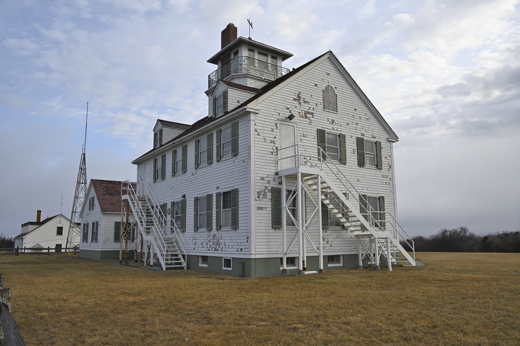 The exterior of a white shingled three story building. There is significant damage to the exterior of the building.