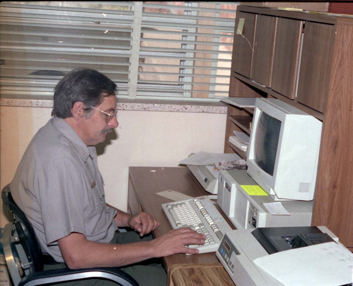 Color Photos of administration personnel. Man seated at computer.