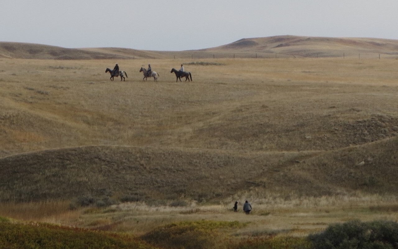 Three horseback riders on distant golden hills,  two people in foreground