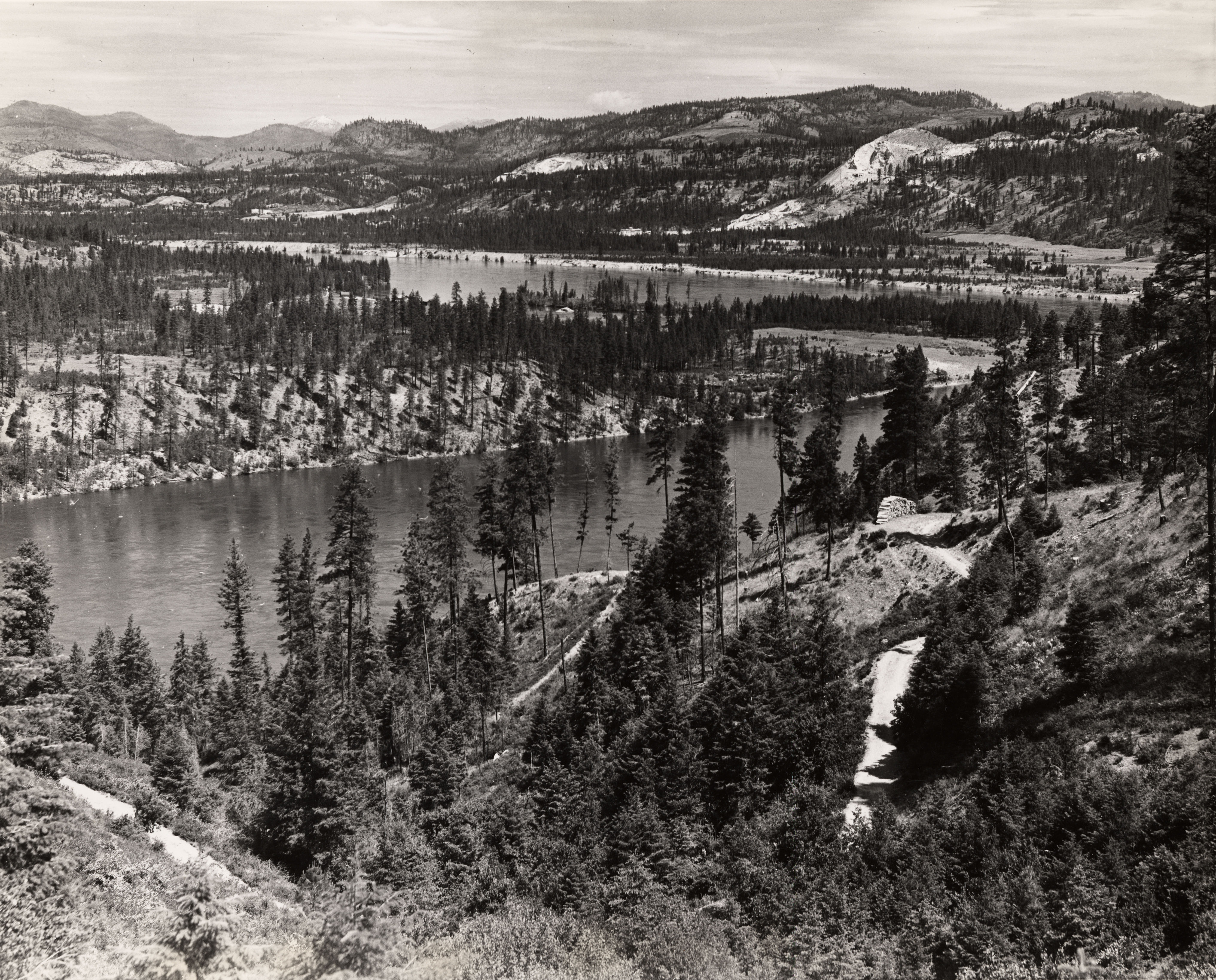 Black and white photograph of a river in a wide forested valley