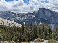 Mountains with partly cloudy skies and trees in foreground.