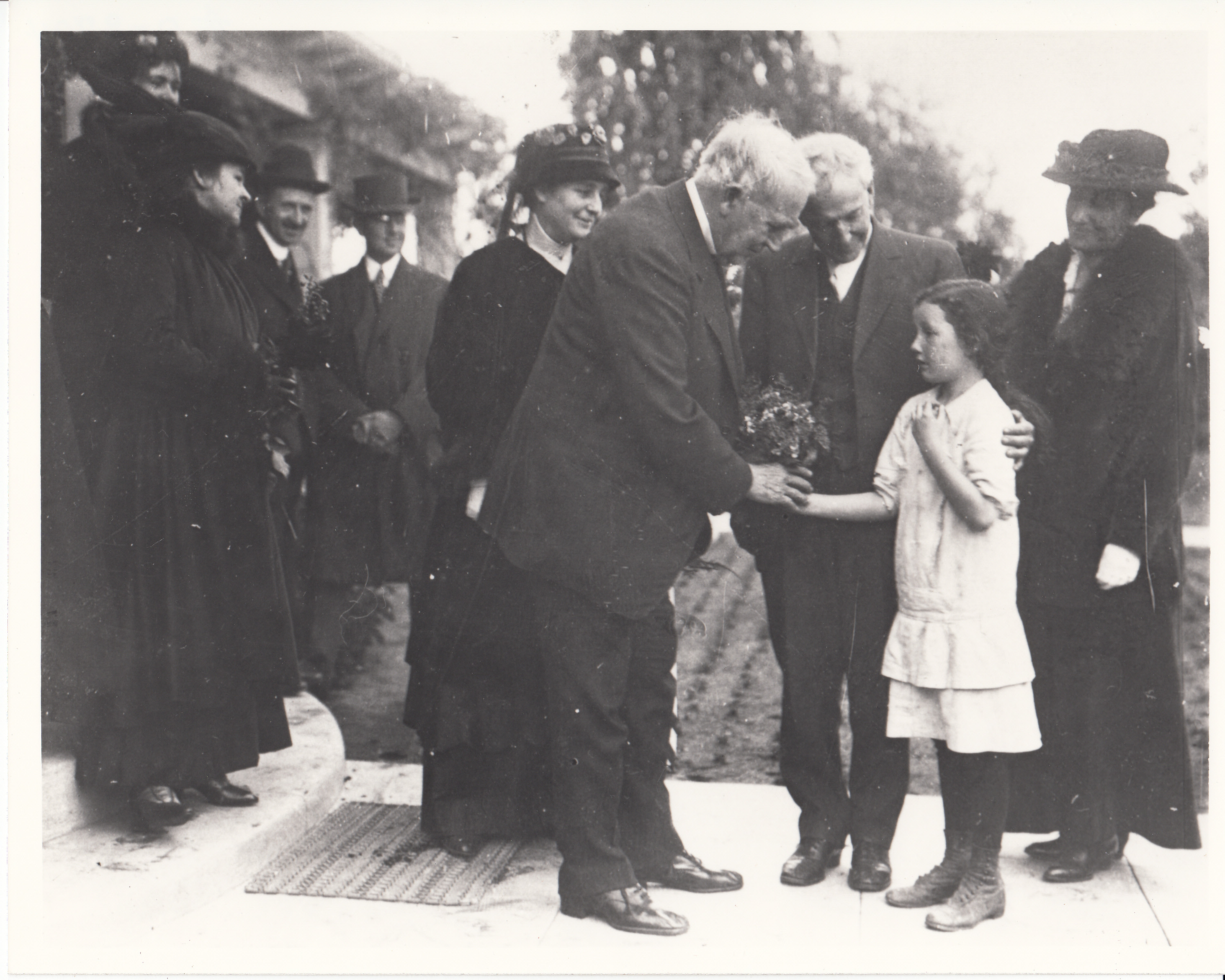Thomas Edison being given flowers by a young girl on California trip. Mina Edison is standing just behind Edison.