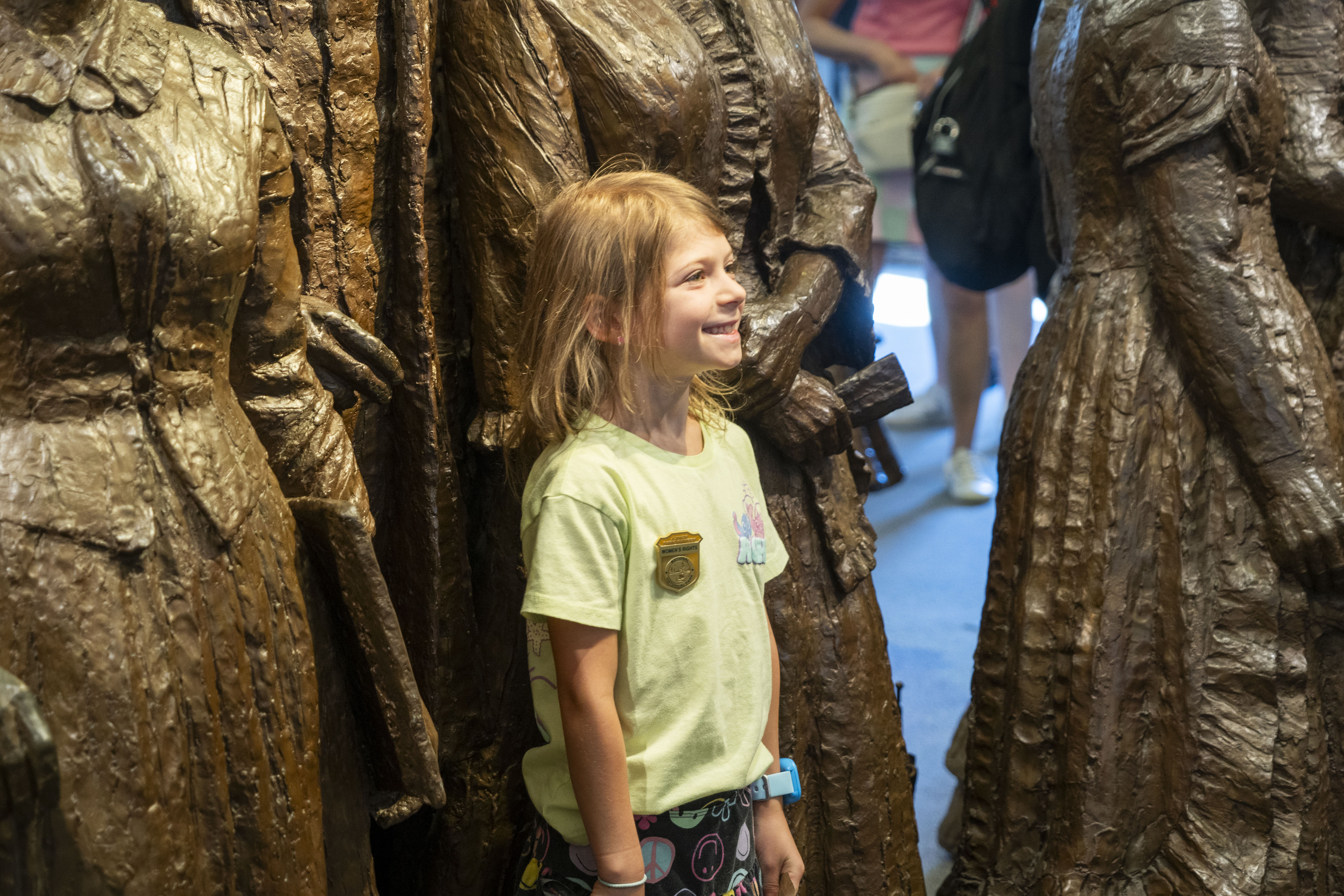 A young child stands and smiles in front of a group of bronze statues