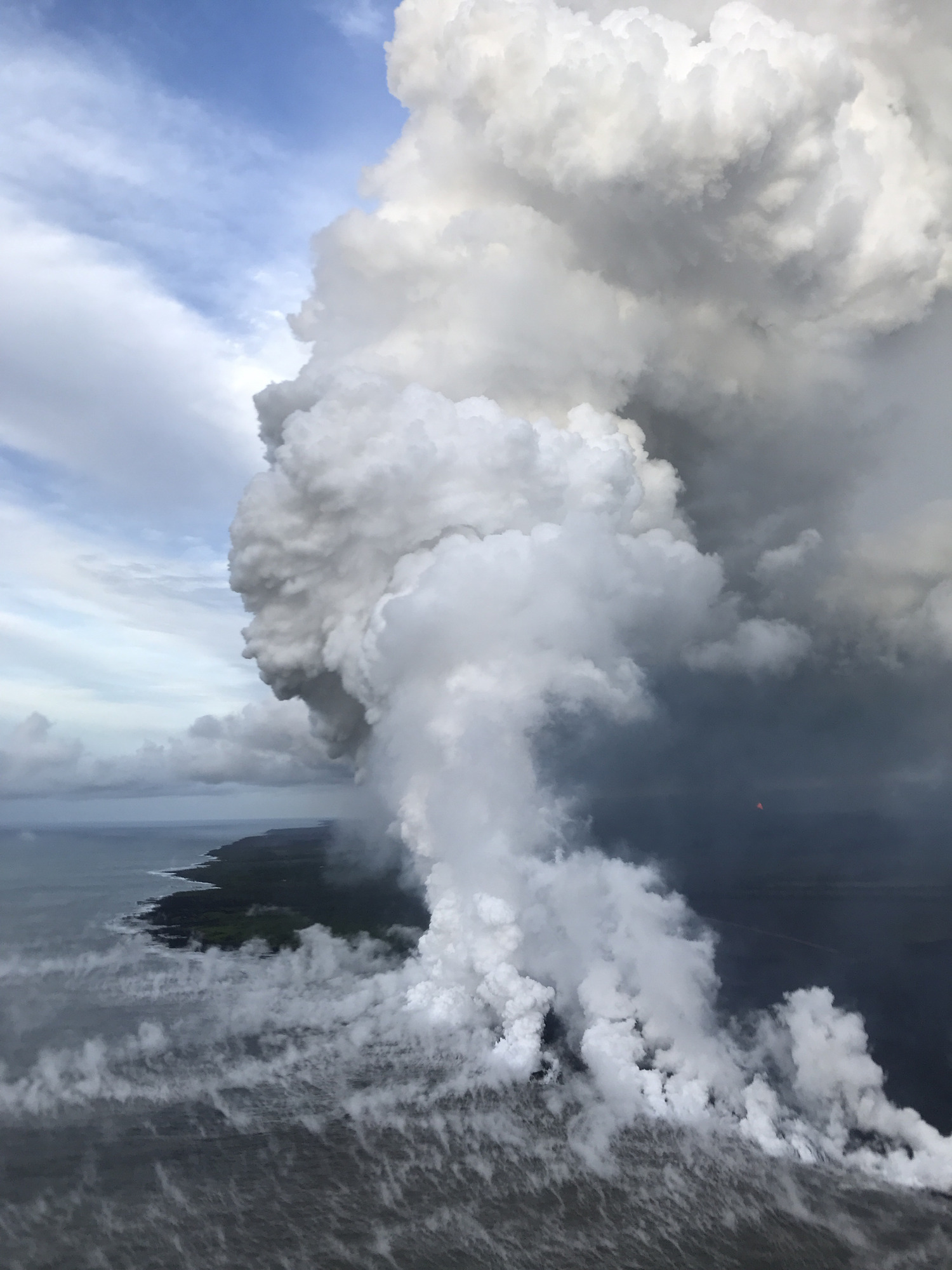 Aerial view of large plumes of steam at the edge of an island