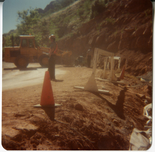 Man monitoring roads with traffic cones and constriction barriers in place behind him.
