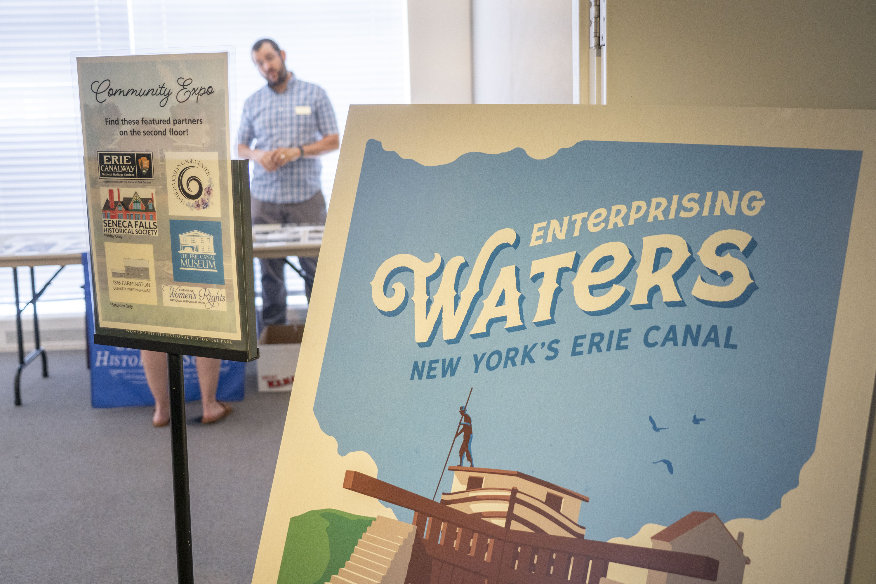 A large blue and white poste rin front of an open door that reads "Enterprising Waters: New York's Erie Canal."