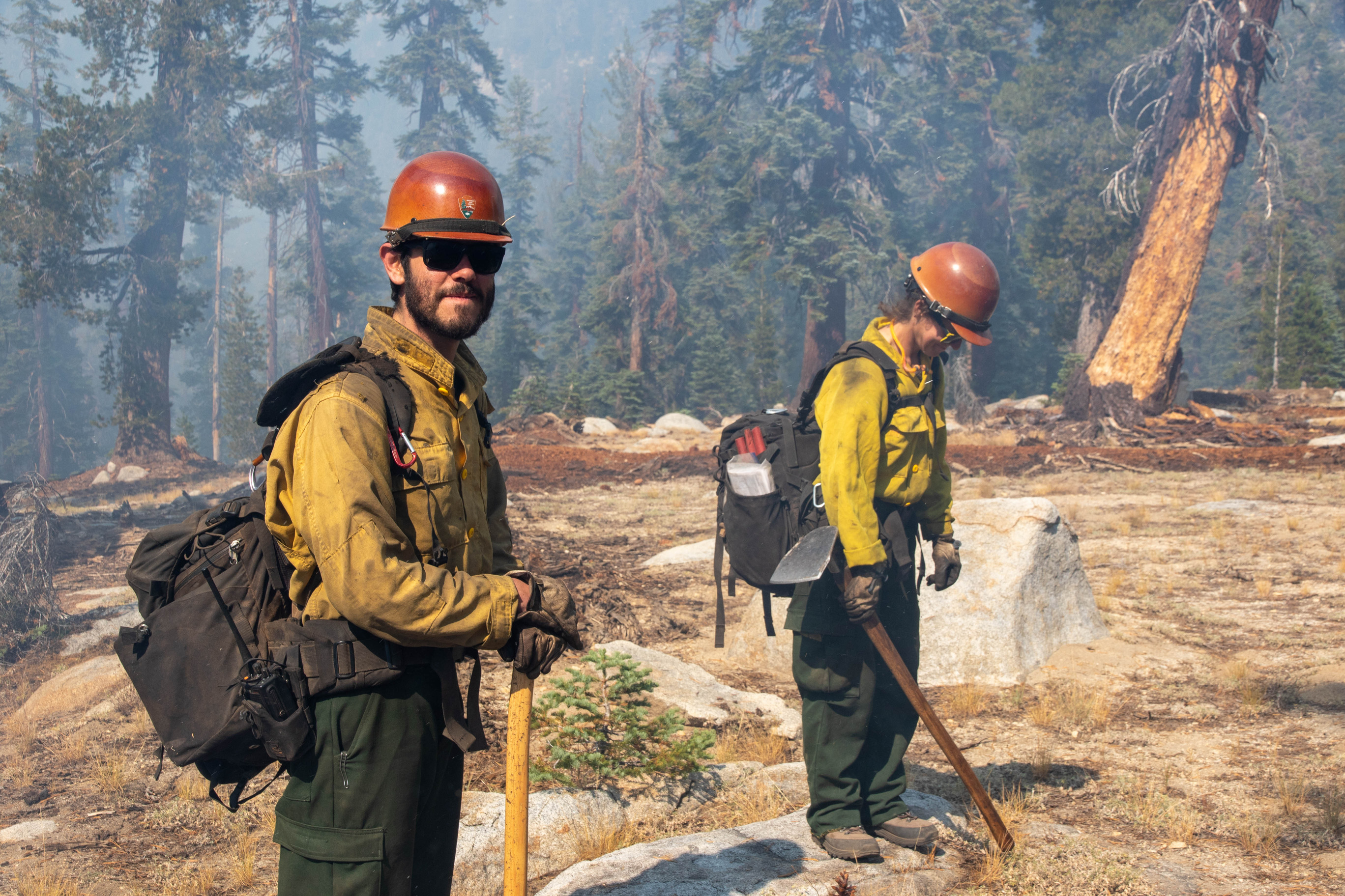 Wildland firefighters walk through wooded areas with smoke and fire around them