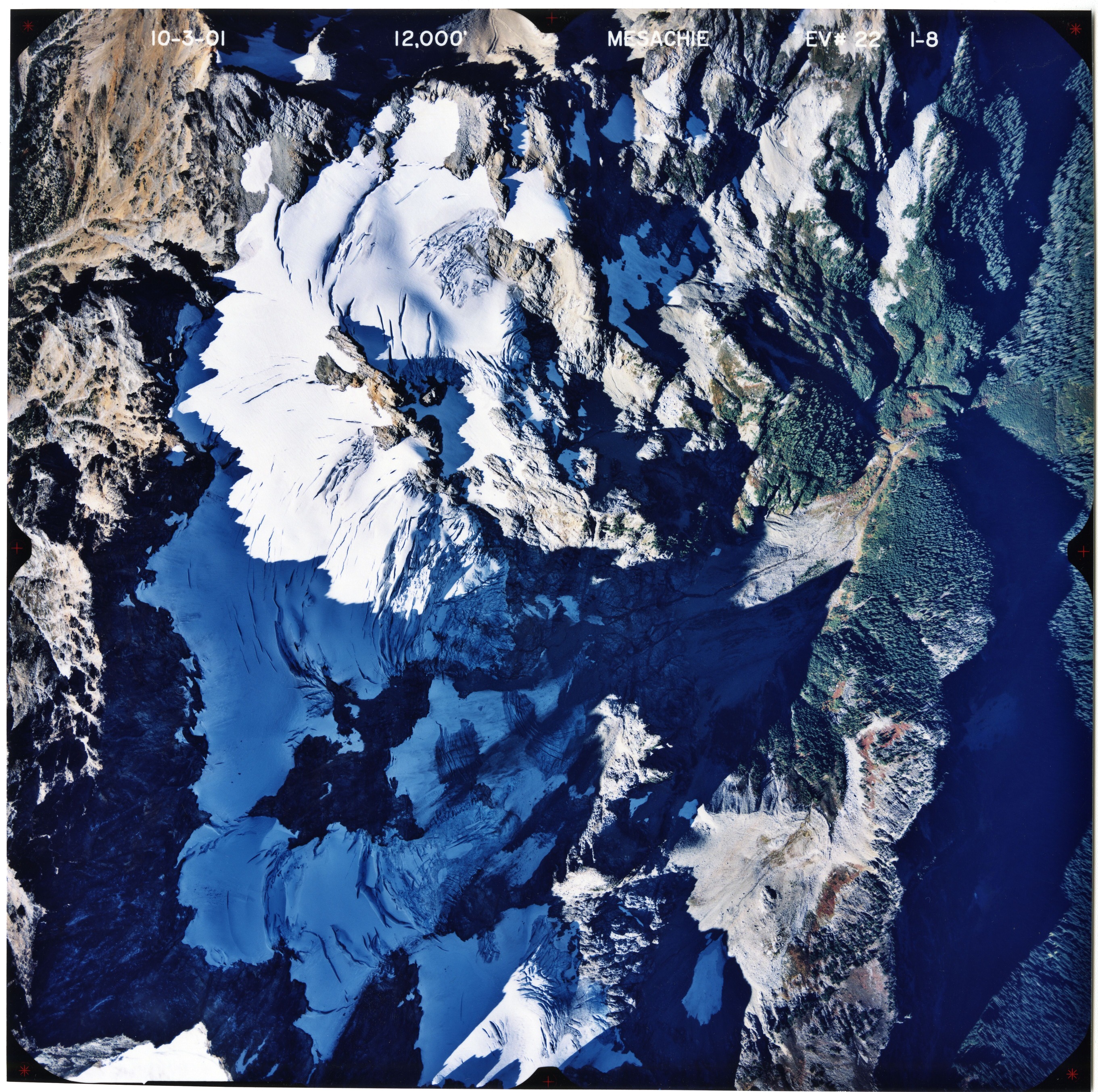 Color aerial photograph of glaciated mountain peak with forested valleys below.