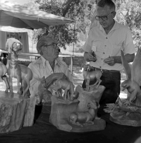 Leo Fesler (seated) with his wood carvings talking with man at third annual Folklife Festival at Zion National Park Nature Center, September 1979.