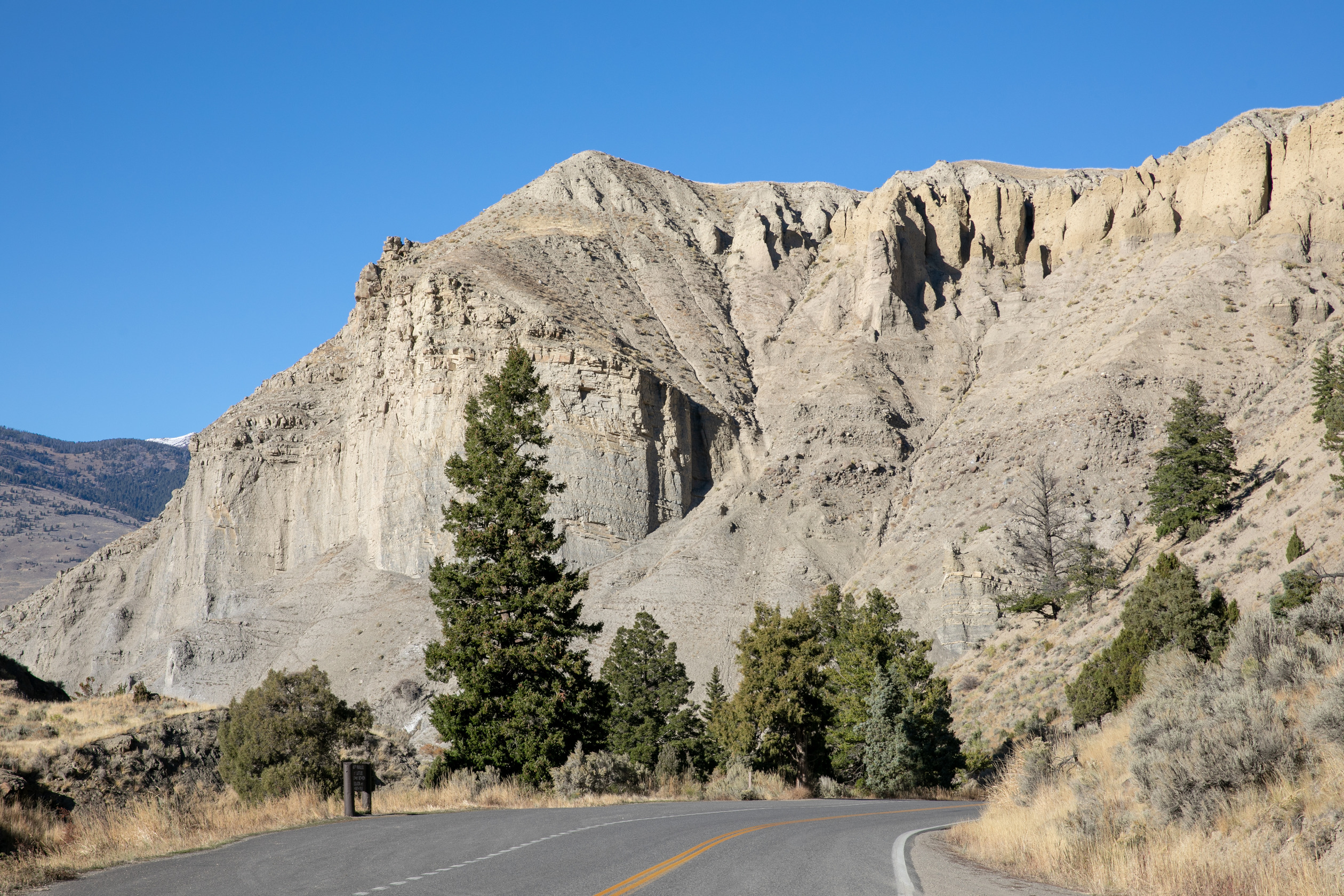Looking from the road up to a cliff with horizontal layers of rock that has eroded into a few gullies