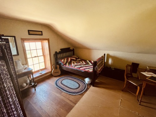 A room with a bed, table, and window. 