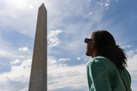 A visitor wearing protective eyewear looks at the partial eclipse over the Washington Monument.