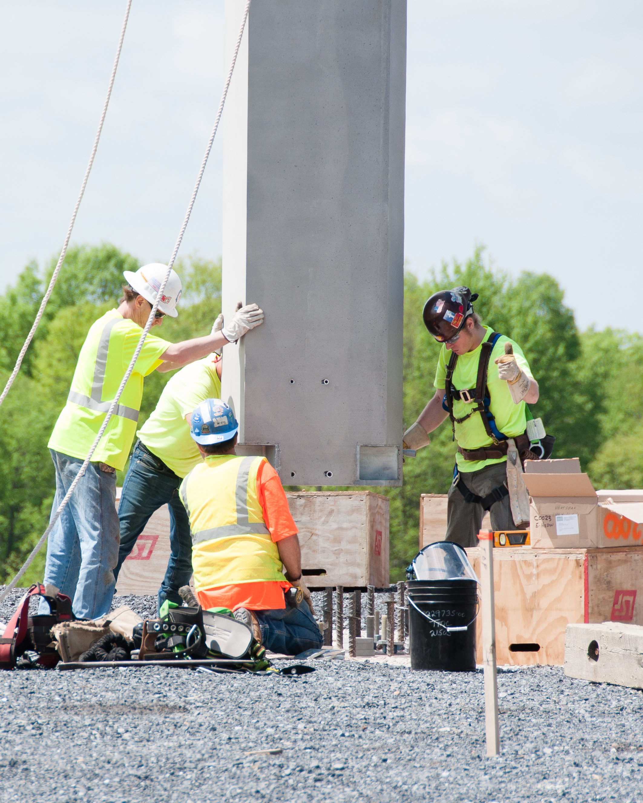 Four men guide a large concrete beam into the tower's foundation. 