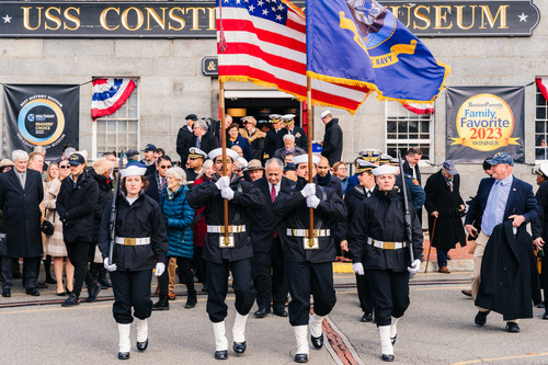 Color guard leads a group of people from a gray stone building.