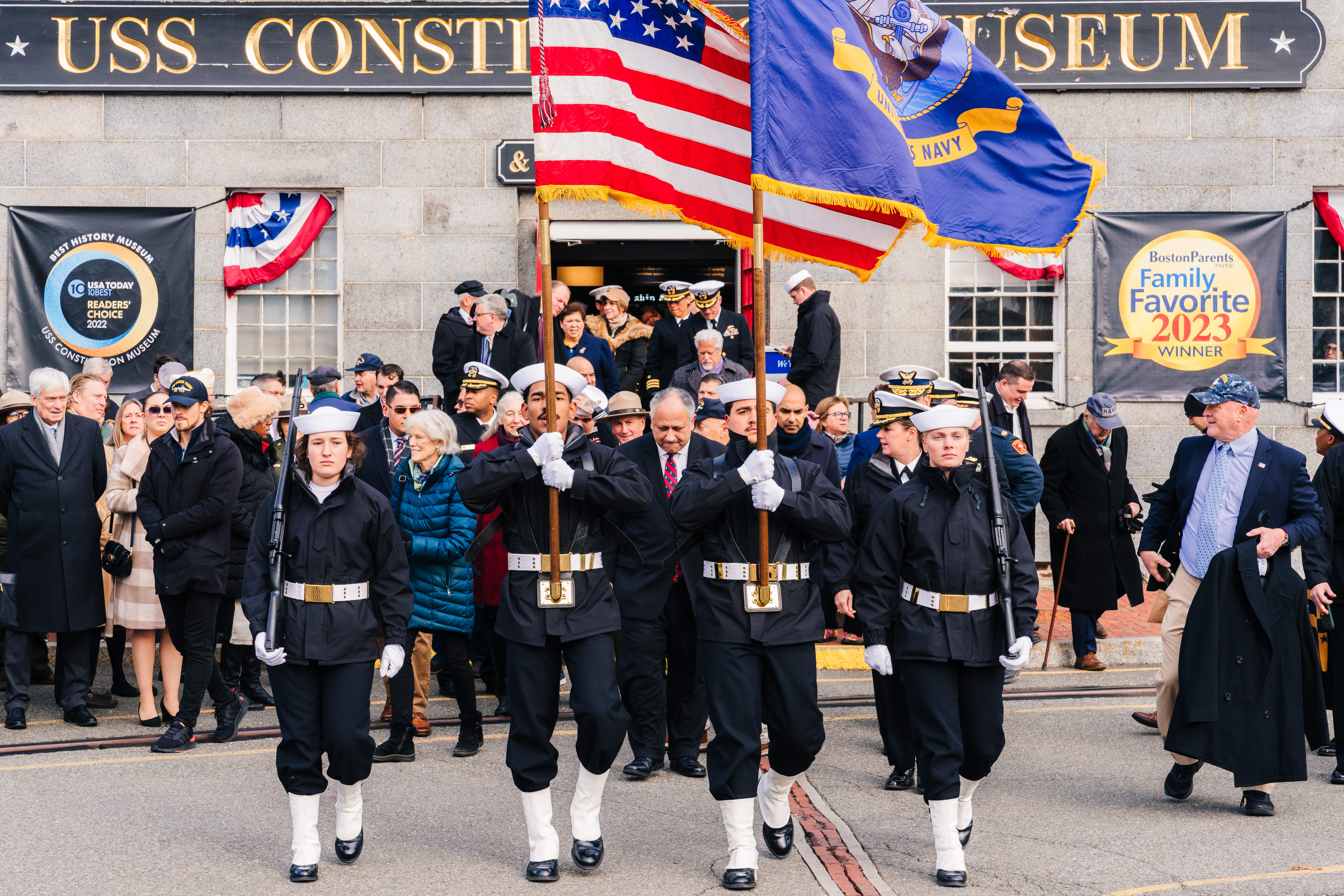 Color guard leads a group of people from a gray stone building.
