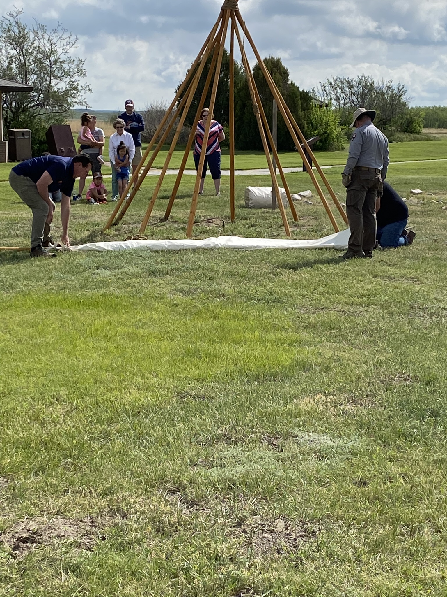 three men about to stretch the canvas over bare tipi poles.