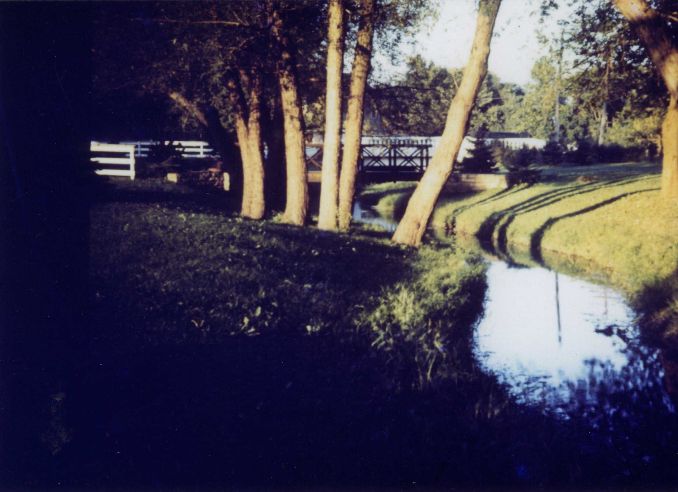 A color photo shows trees and white rail fences near a rural creek. 