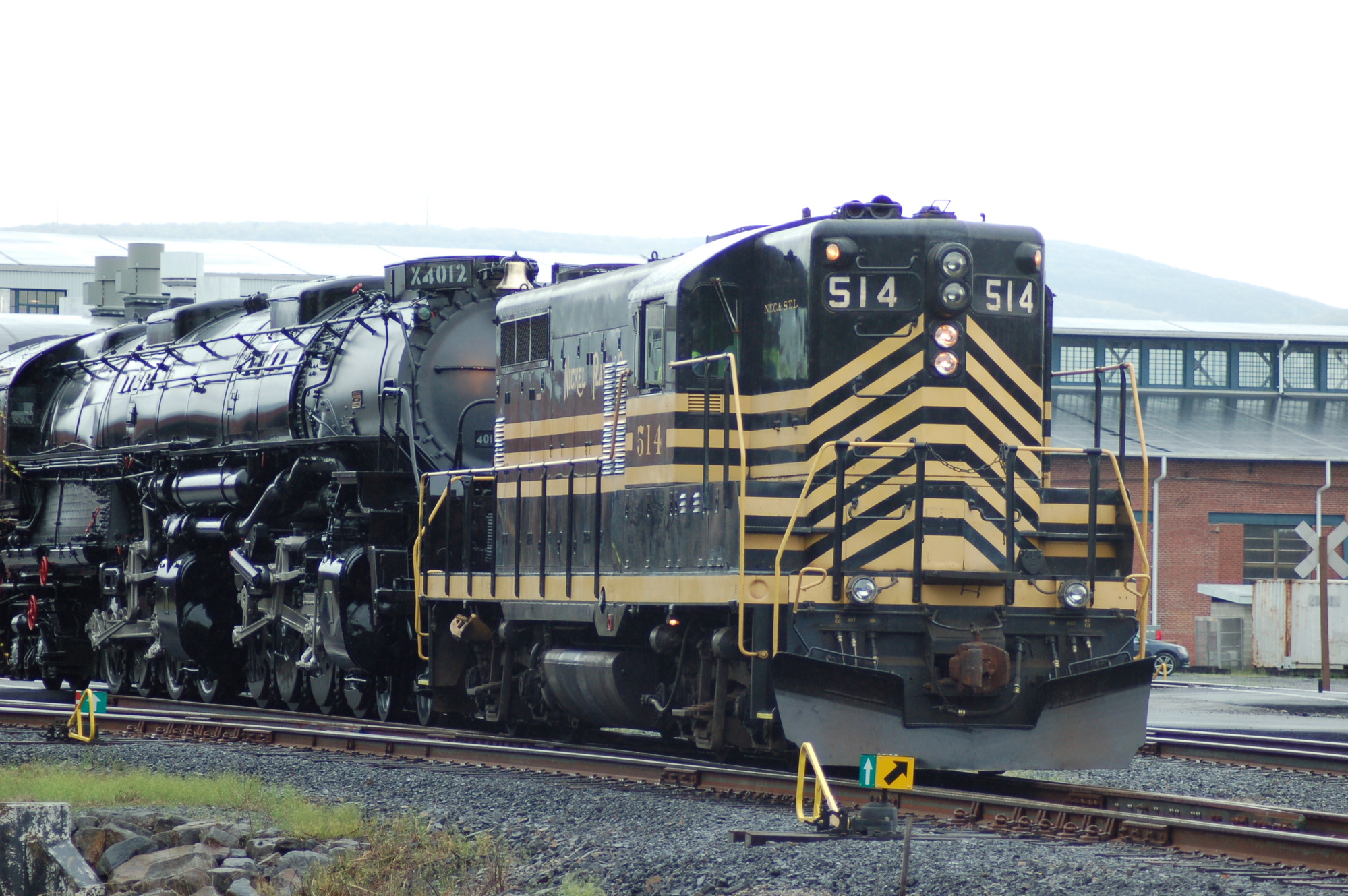Black train with horizontal yellow stripes and the number 514 pulling a larger black train on tracks
