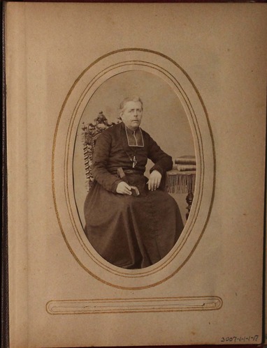 Black and white photograph of man seated at desk in clerical garb.