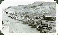 This is an historic black and white photograph from the Scotty's Castle Historic Photograph Collection, Death Valley National Park of Scotty's Castle Watercourse and road leading east to Stables. Fire Cache on right. January 16, 1931. Photographed by Mat Roy Thompson.