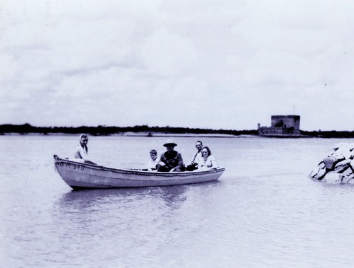 5 people in a small boat.  Fort in the background.