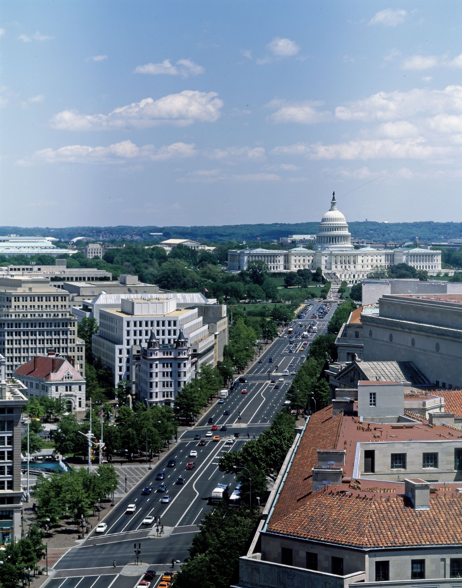 A six lane black-topped road stretching from the lower left to the upper right. A large white building, topped with a large dome, the US Capitol, is at the far end of the road. 