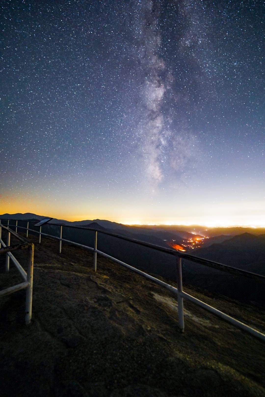 stars in a dark blue sky over a mountain landscape with handrails