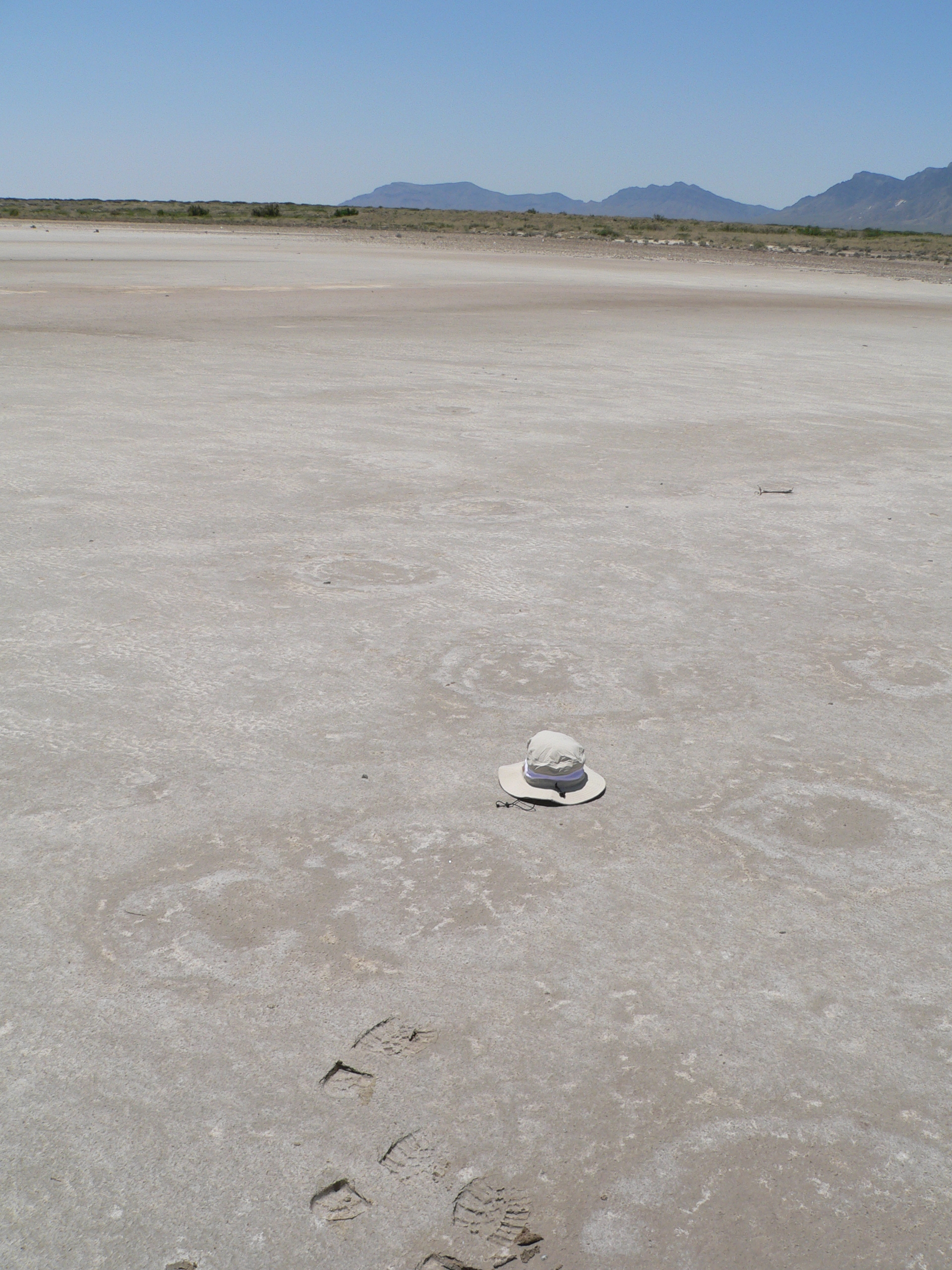 a wide sand field with several circular shapes in it. A sun hat sits in the middle of the field. 