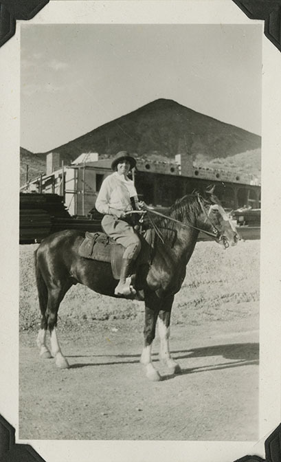 This is an historic black and white photograph from the Scotty's Castle Historic Photograph Collection, Death Valley National Park of Edna Devlin on horseback with Scotty's Castle Hacienda under construction in background. Circa 1930.