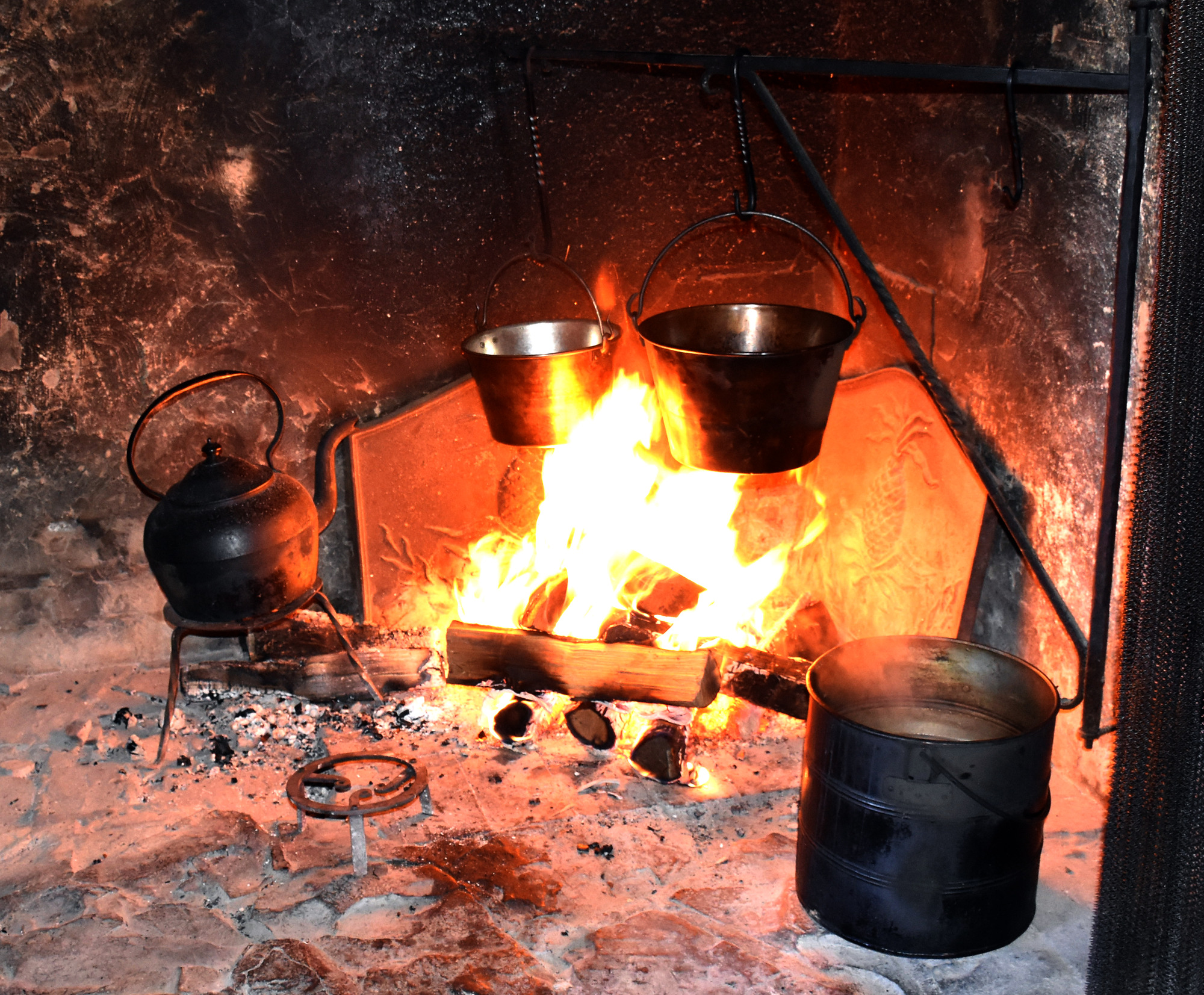 Several metal pots hang over or are positioned near a cooking fire.