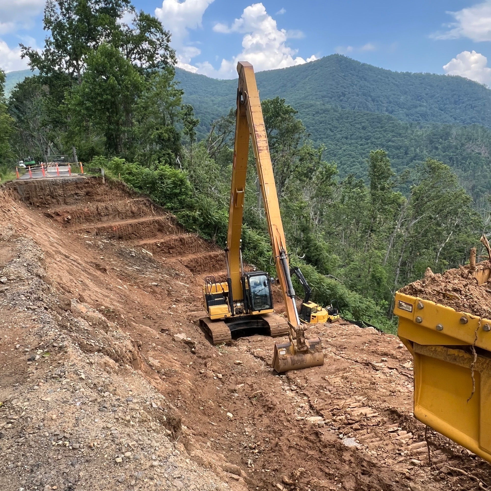 An excavator removes dirt on the side of a slope to stabilize and repair damage from a slide caused by hurricane Helene at milepost 375.