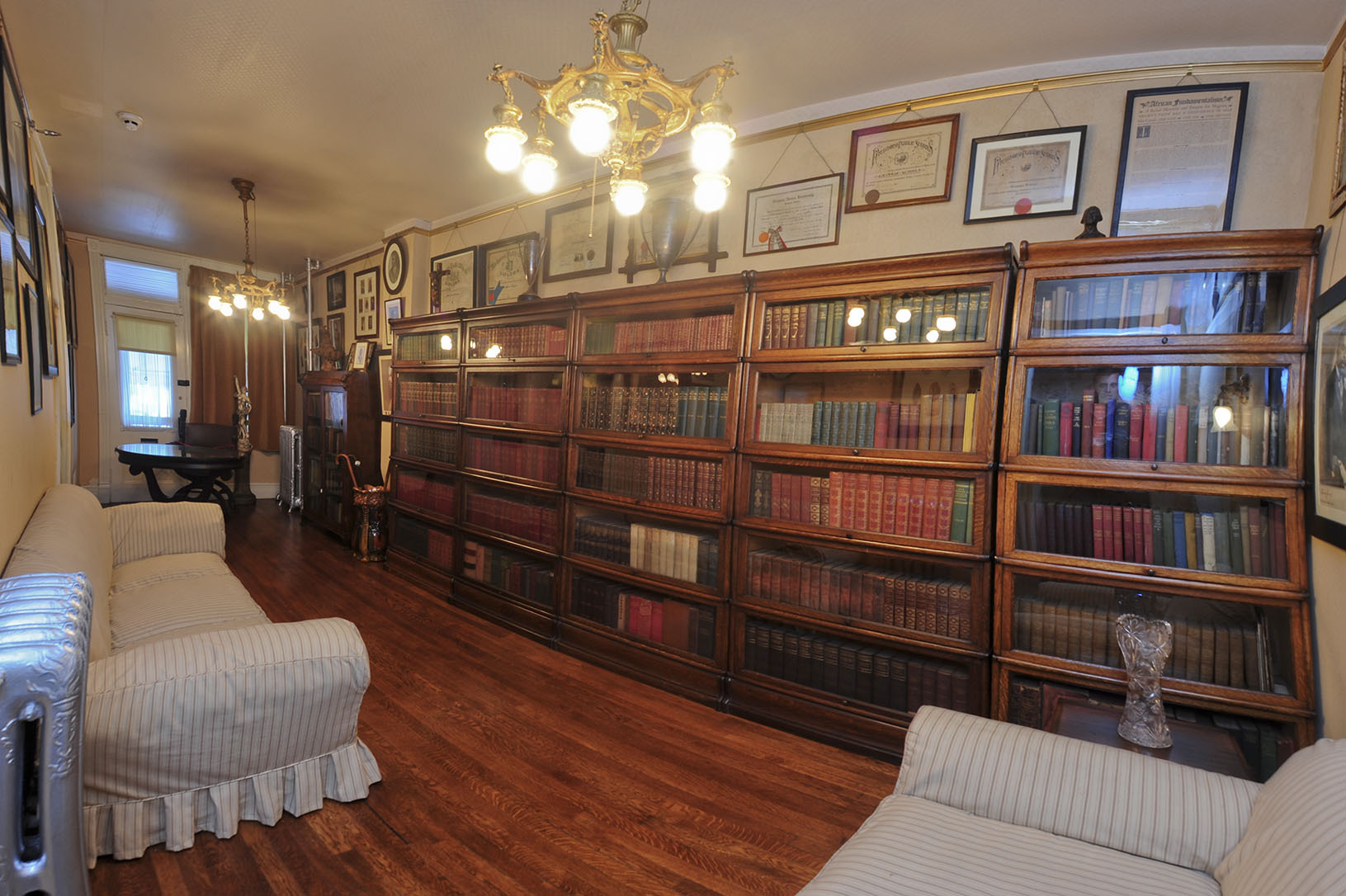 Large bookcases with over 600 books cover a full wall, a couch opposite the bookcase and a table and chair at the far end of the room.