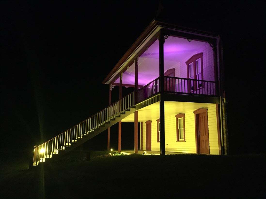 Two-story porch lit purple and gold at night