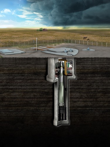 Photo Description: An area of gravel in the middle of a prairie. Under a concrete pad, a missile rests in a hole while a storm brews on the horizon.