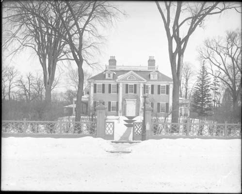 Black and white photograph of Georgian mansion, front fence visible and lawn covered in snow.